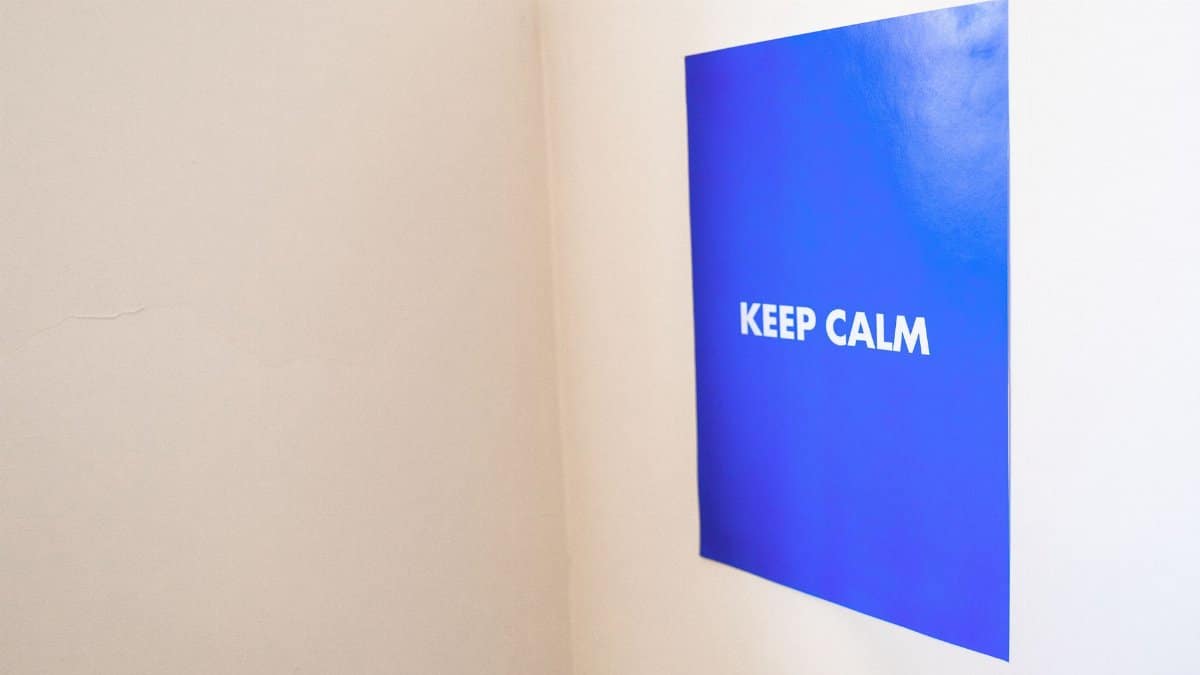 A minimalist blue poster displaying the text 'Keep Calm' on a white wall, offering a calming visual.