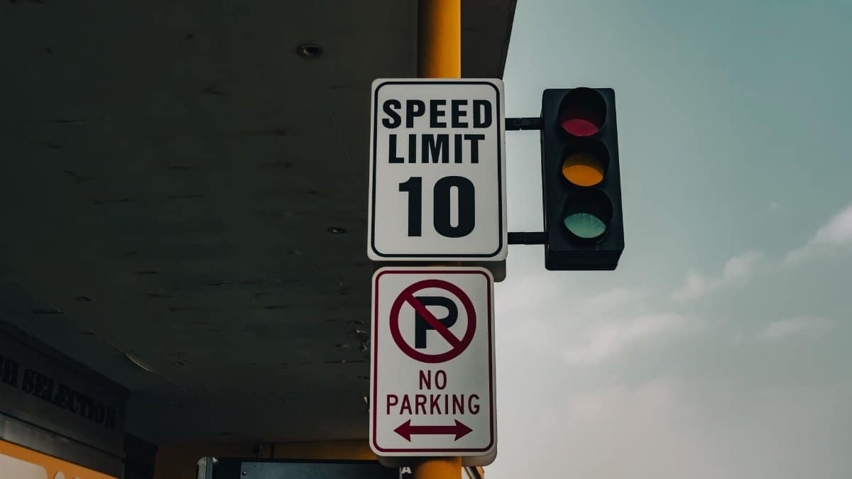 Close-up of a speed limit sign and traffic lights at an intersection under a cloudy sky.