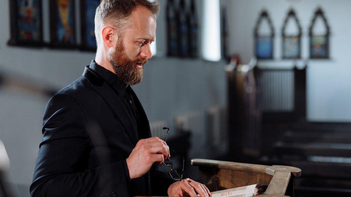 A priest stands at a pulpit, delivering a sermon in a church setting.