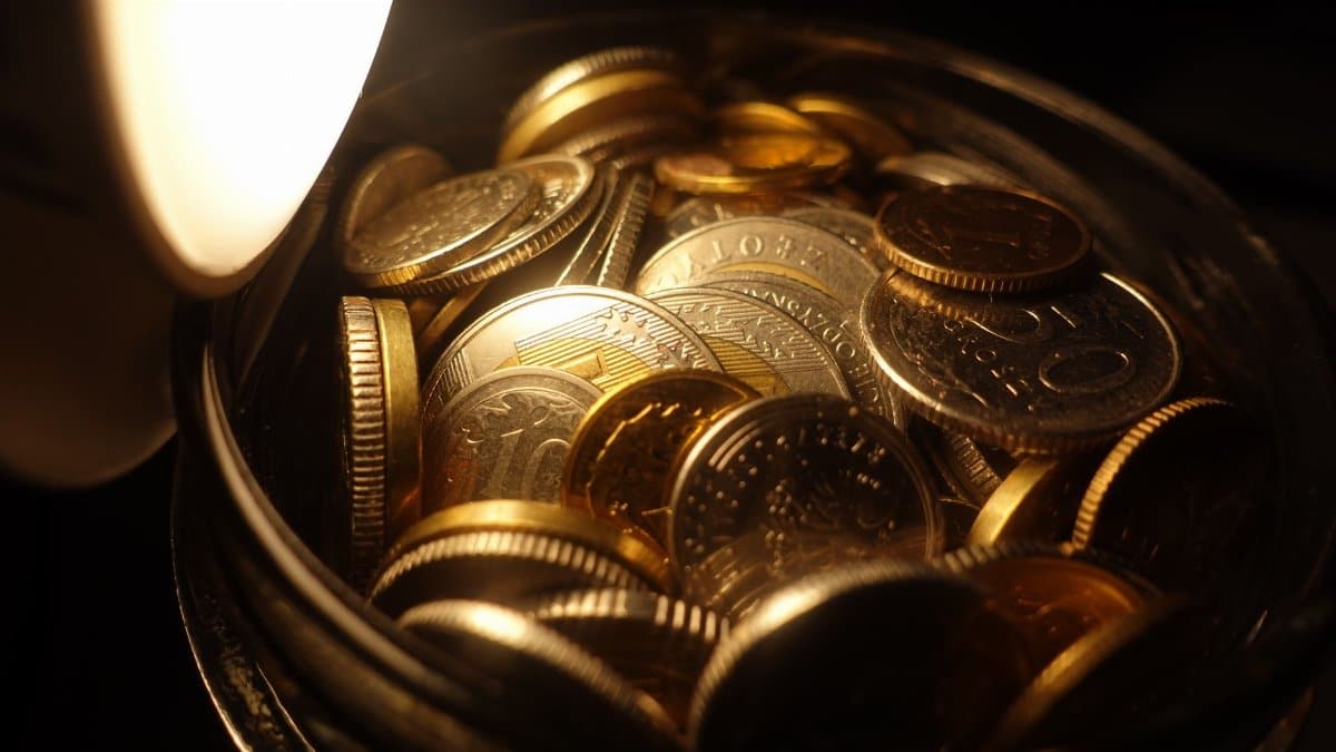 A detailed view of assorted coins in a jar under warm light, depicting financial wealth.