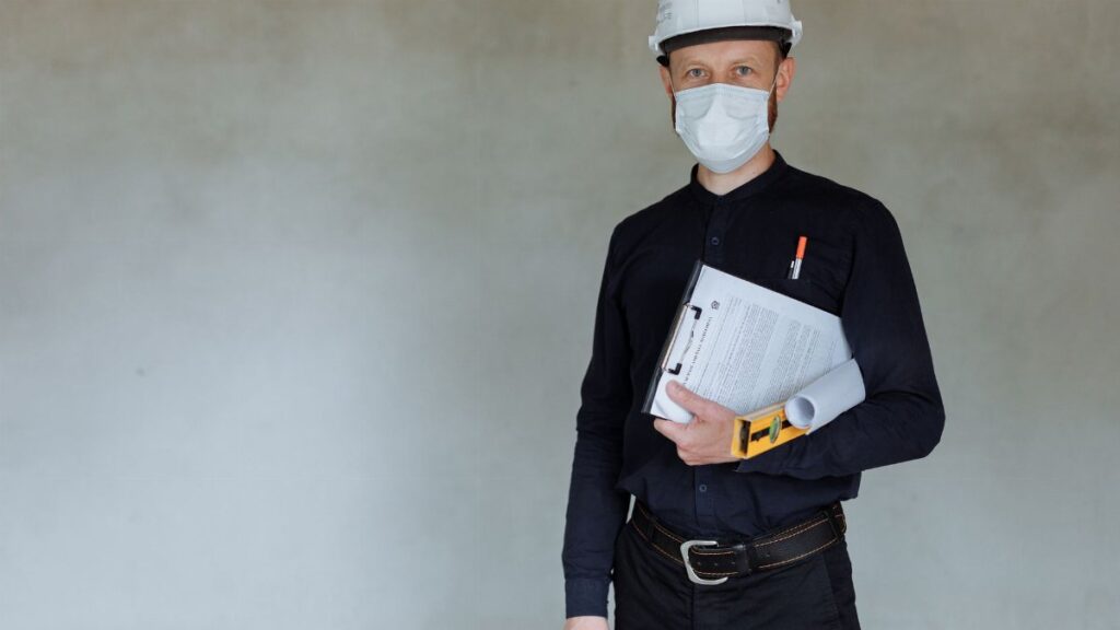 Construction worker wearing safety gear and holding documents during pandemic.