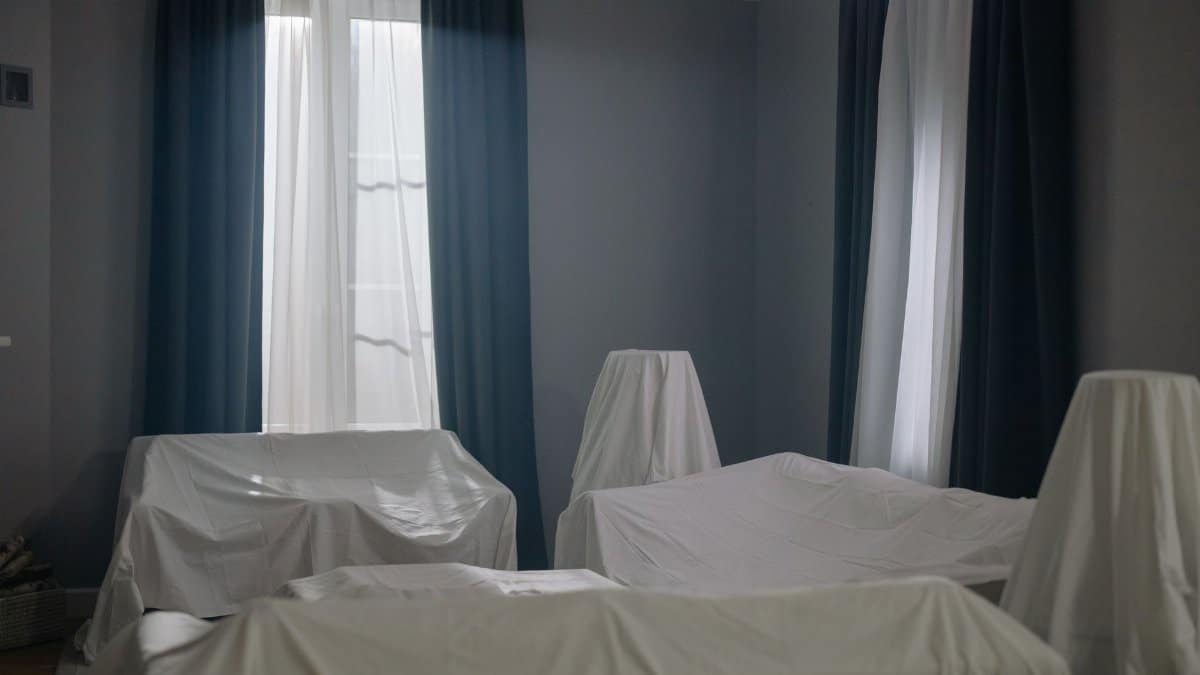 A dimly lit room with furniture covered with white sheets, suggesting an unused space.
