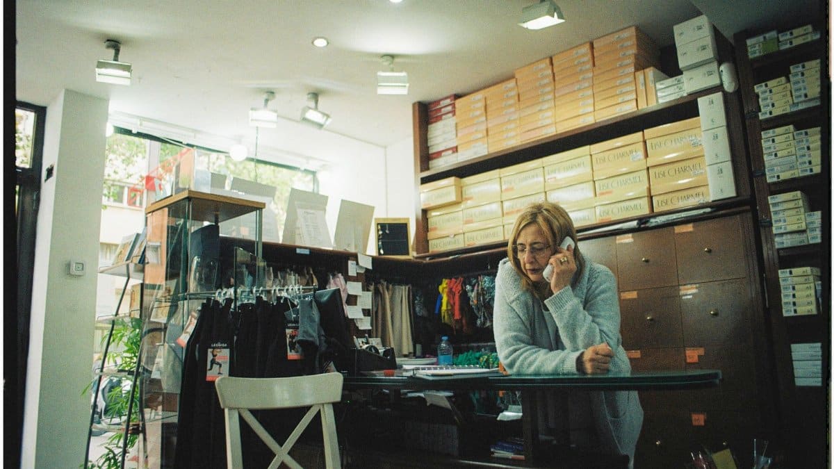 Woman working in a clothing store, talking on the phone near merchandise racks.