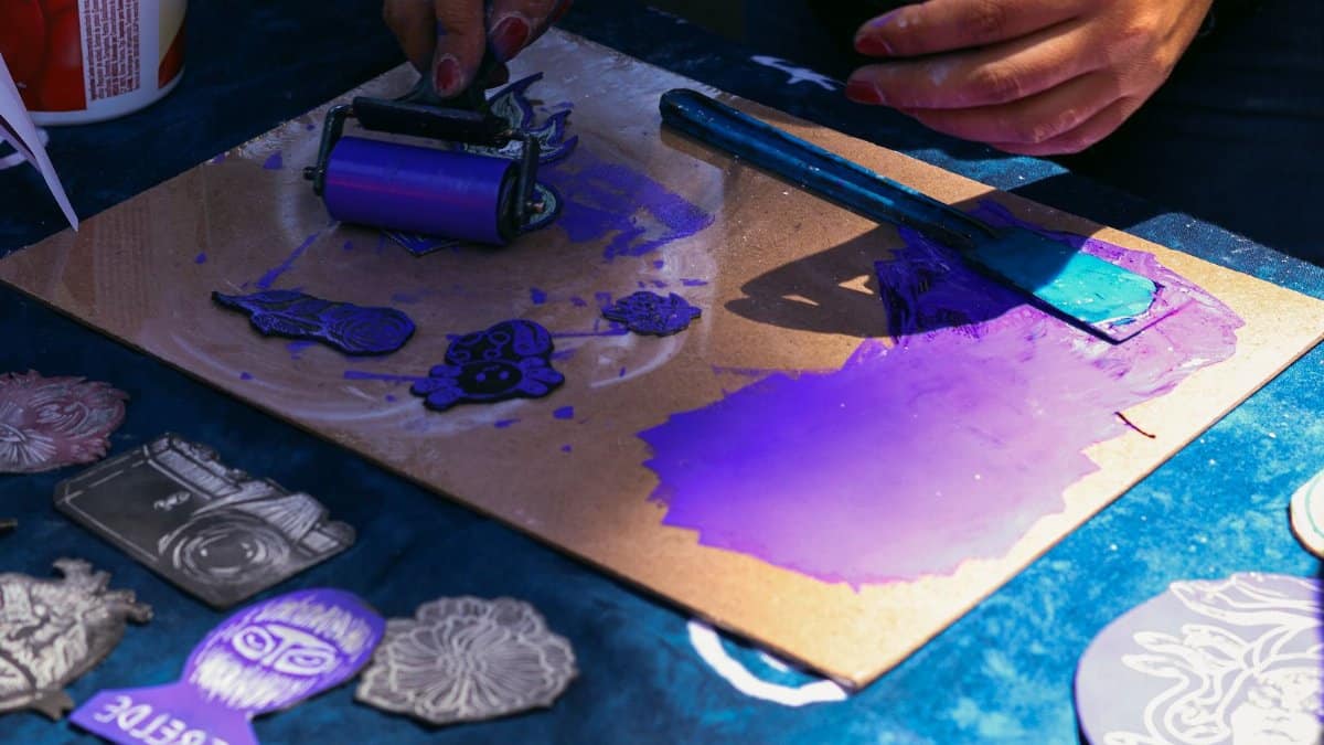 Artist working with purple ink on linocut prints. Hands engaged in creative process with vibrant colors.