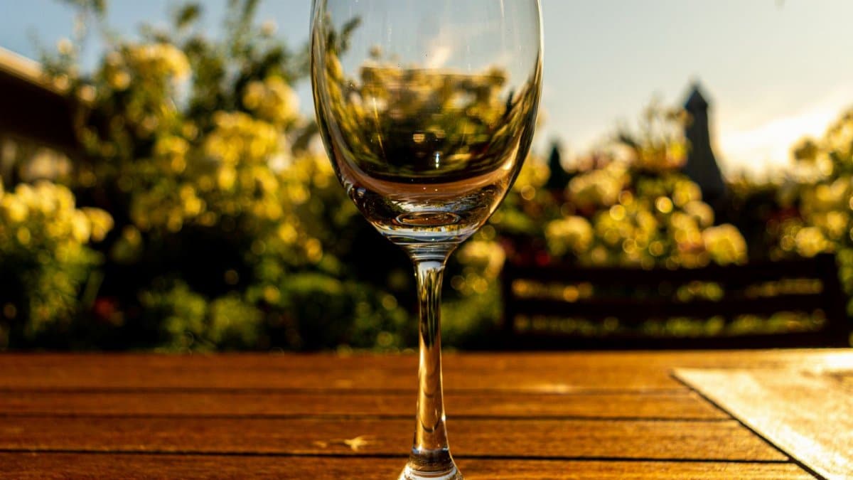 An empty wine glass sits on a wooden table in a sunny French garden, perfect for summer relaxation.