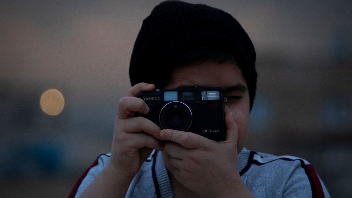 A young person captures a moment with a vintage camera, set against an urban backdrop.