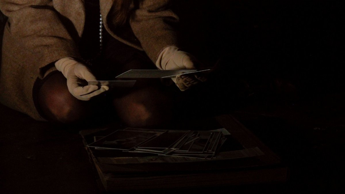A person wearing gloves examines photographs in a dark and mysterious setting.