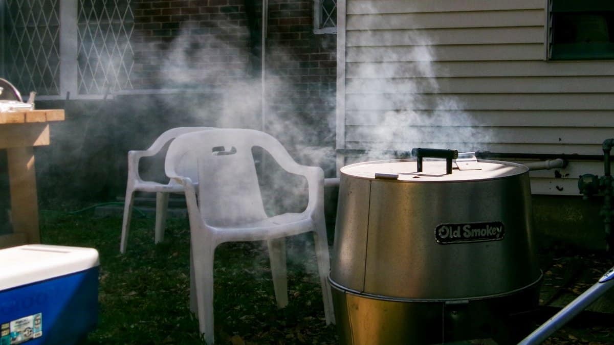 Smoke rising from a barbecue grill beside empty chairs in a Houston backyard setting.