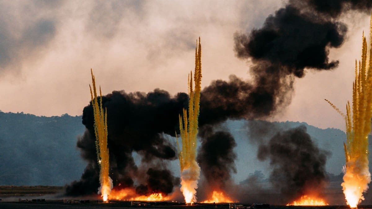 Intense scene of fire eruptions and smoke plumes rising against a cloudy sky, creating a dramatic atmosphere.