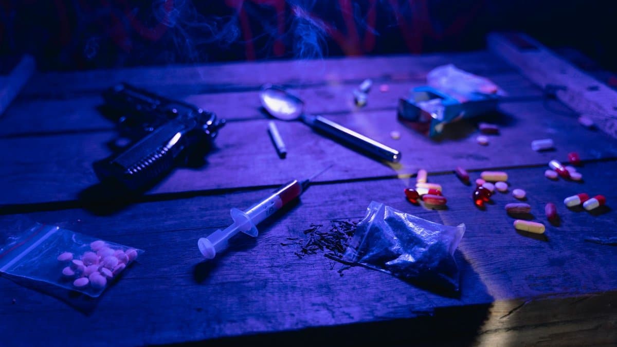 A moody scene displaying drugs, a gun, and smoke under dramatic lighting.