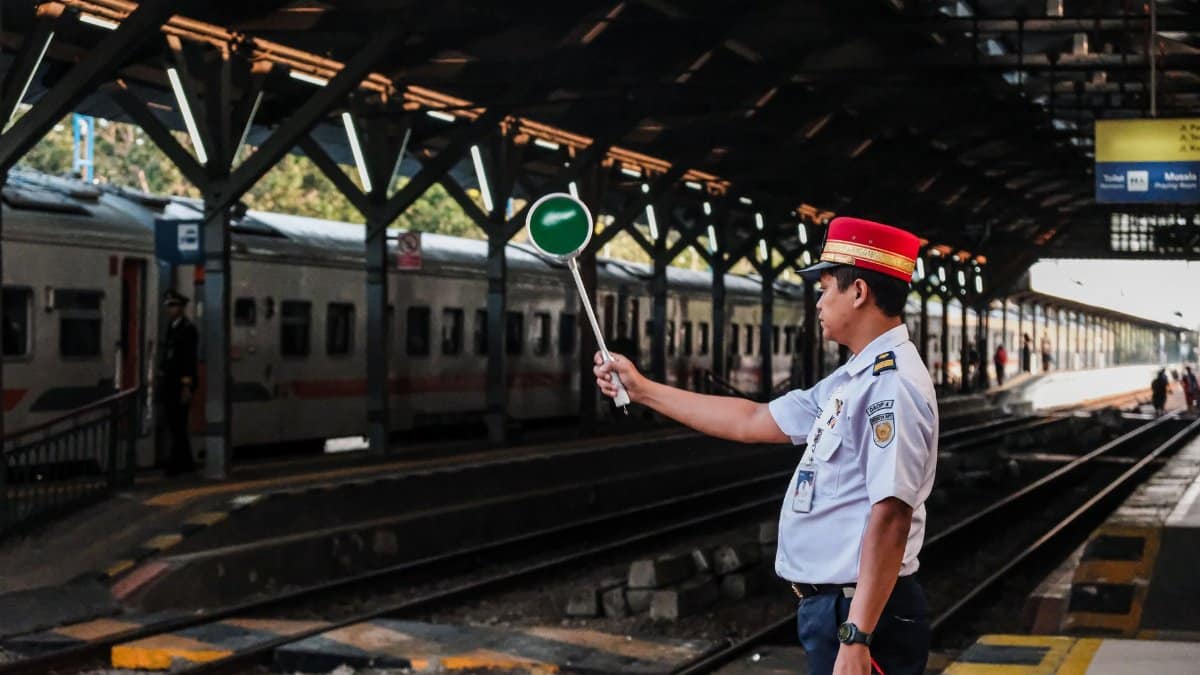 Train station guard holding a signal paddle on a station platform, ready for train departure.