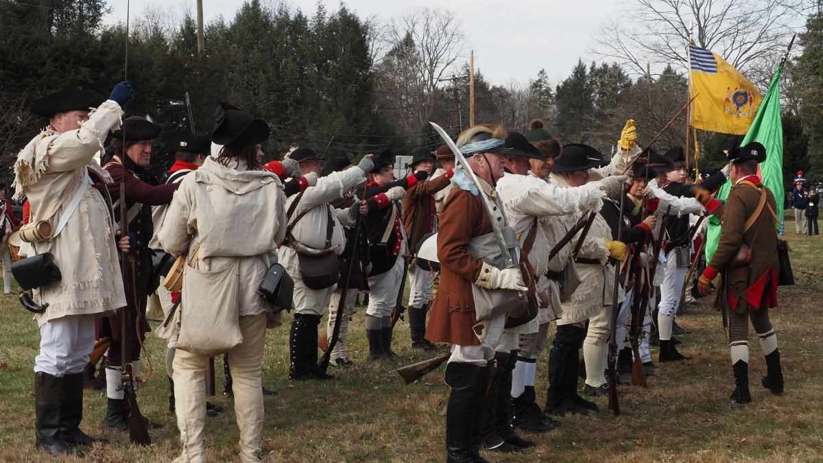 Reenactors in colonial attire perform a Revolutionary War battle re-enactment outdoors.
