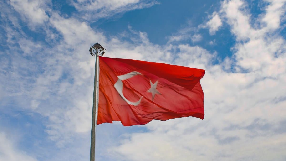 Turkish flag waving proudly against a bright blue sky with scattered clouds, symbolizing national pride.