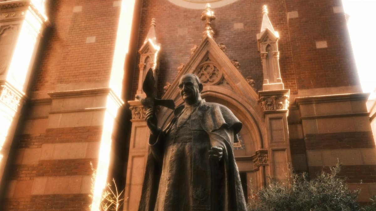 A bronze statue of a pope stands before a historic cathedral with ornate architecture.