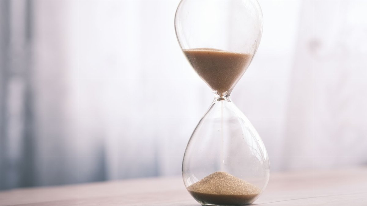Minimalist hourglass filled with sand symbolizing time and patience, against a soft background.