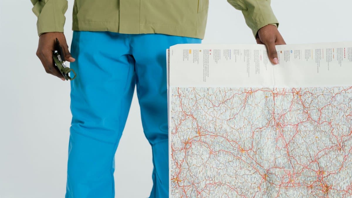Man in outdoor attire holding a map and compass, prepared for exploration.