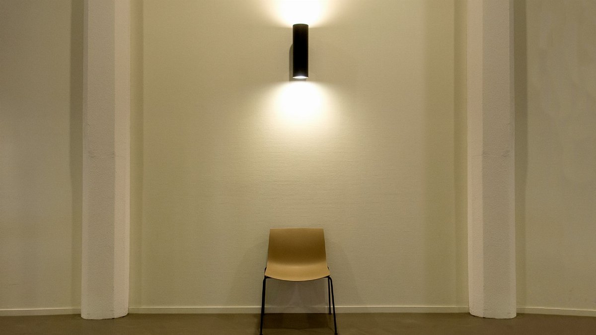 A single chair under a modern wall lamp in a minimalist interior setting.