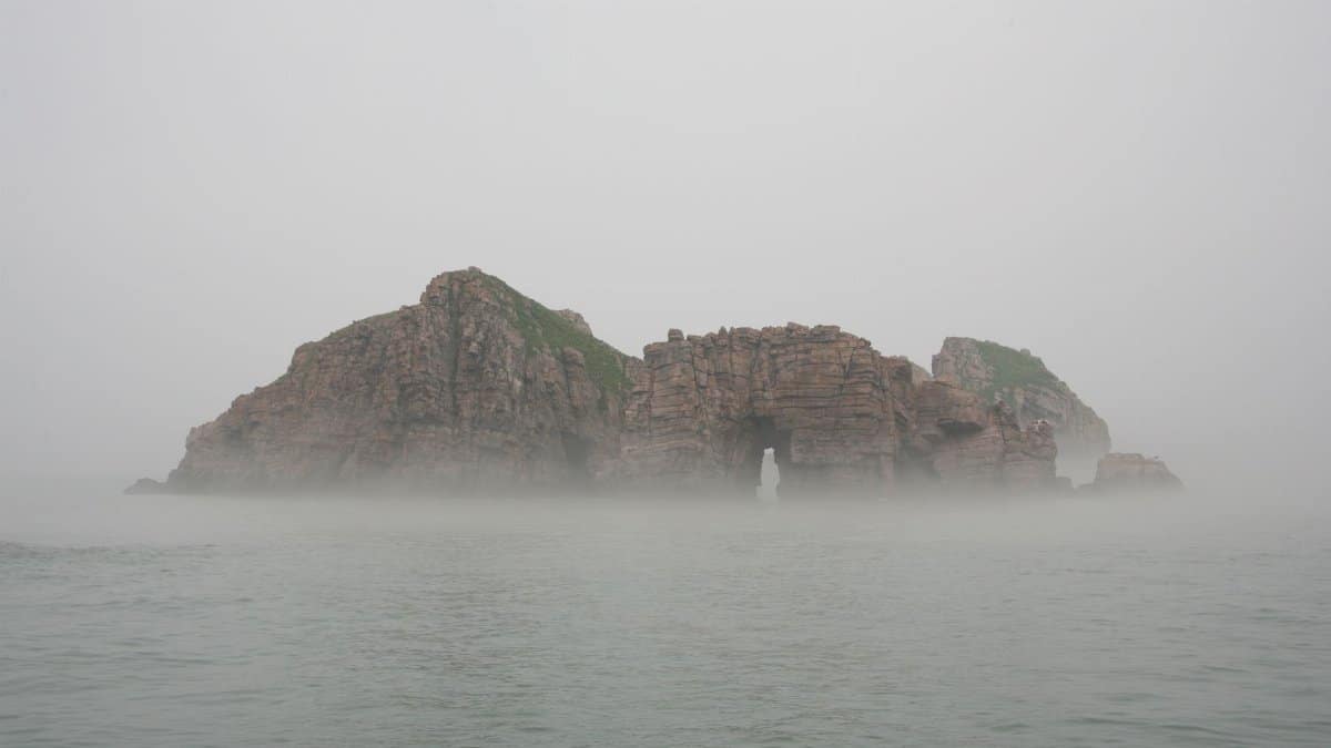 Ethereal view of a rocky island surrounded by mist and sea, creating a serene and mysterious atmosphere.