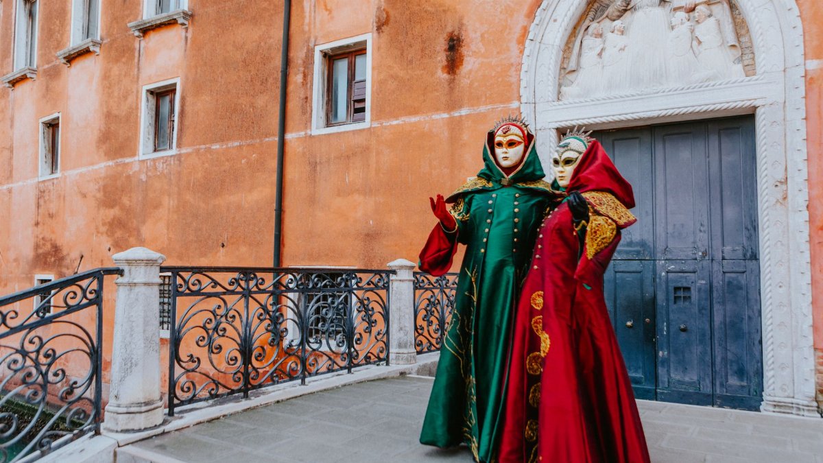 Two people in ornate Venetian costumes and masks standing outside an old building in Venice.