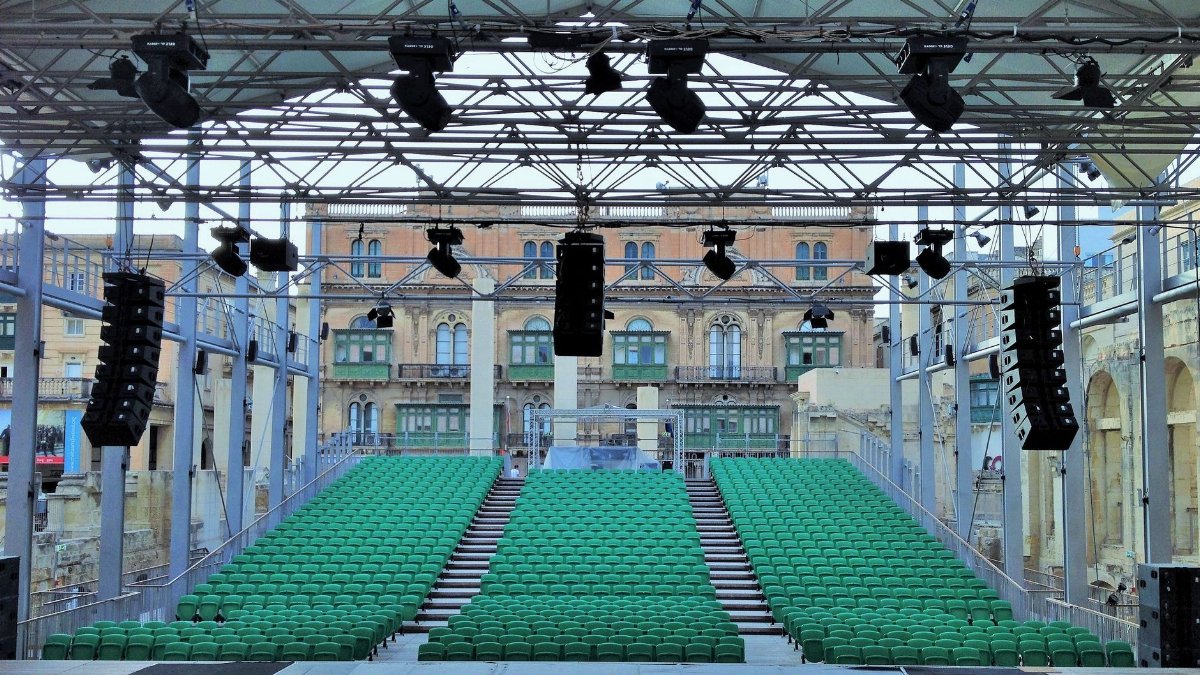 Empty seats and stage with modern light and sound equipment mounted on city square near aged buildings on sunny day