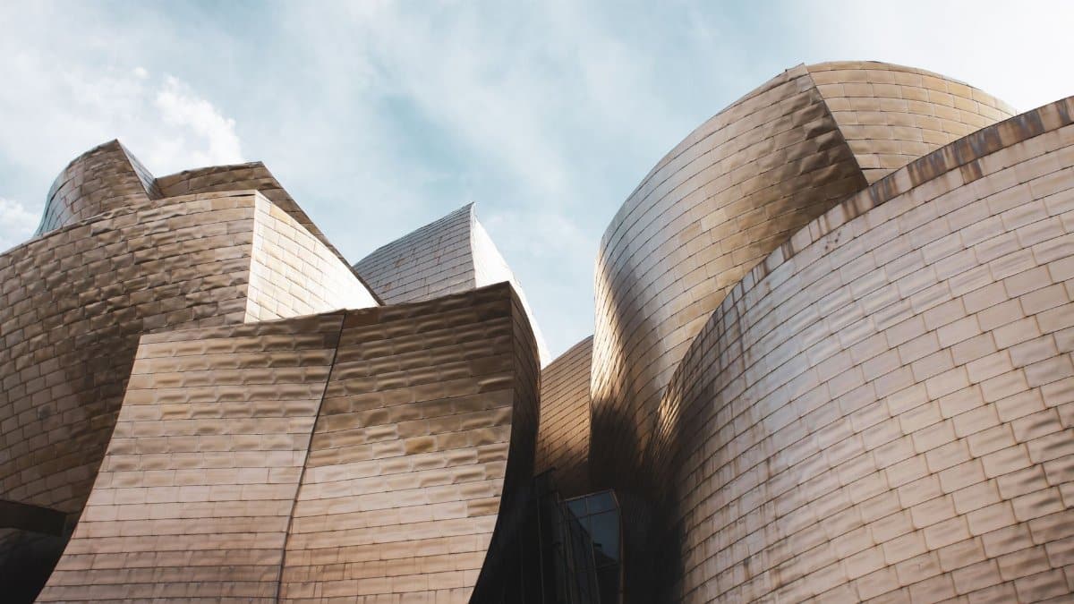 Low angle view of Guggenheim Museum Bilbao's modern architecture under a bright sky.