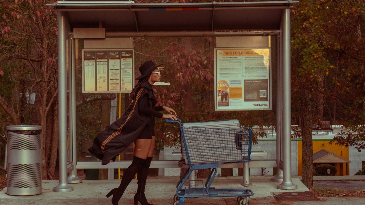 Stylish woman pushing a cart at an outdoor Atlanta bus stop in fall season.