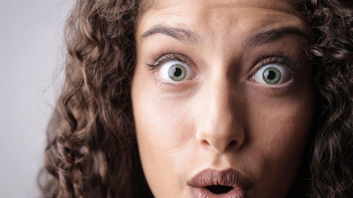 Close-up portrait of a woman with curly hair expressing surprise, highlighting her beautiful eyes and lively expression.