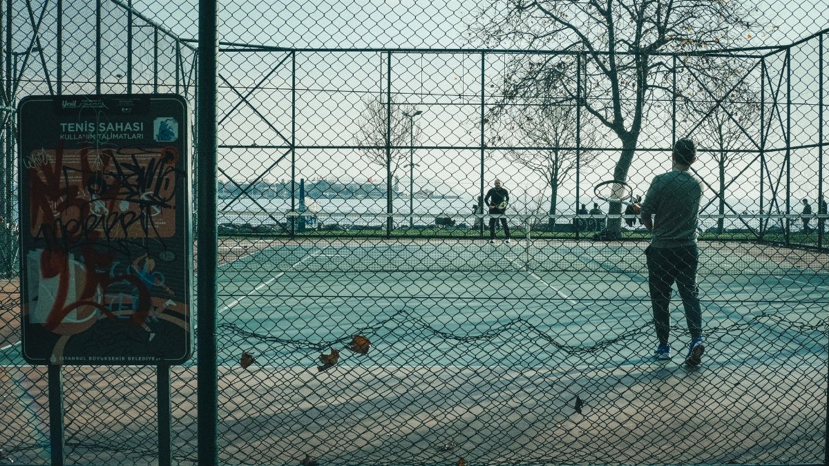 Two players engage in a tennis match on an outdoor court in Istanbul, with a scenic water view.