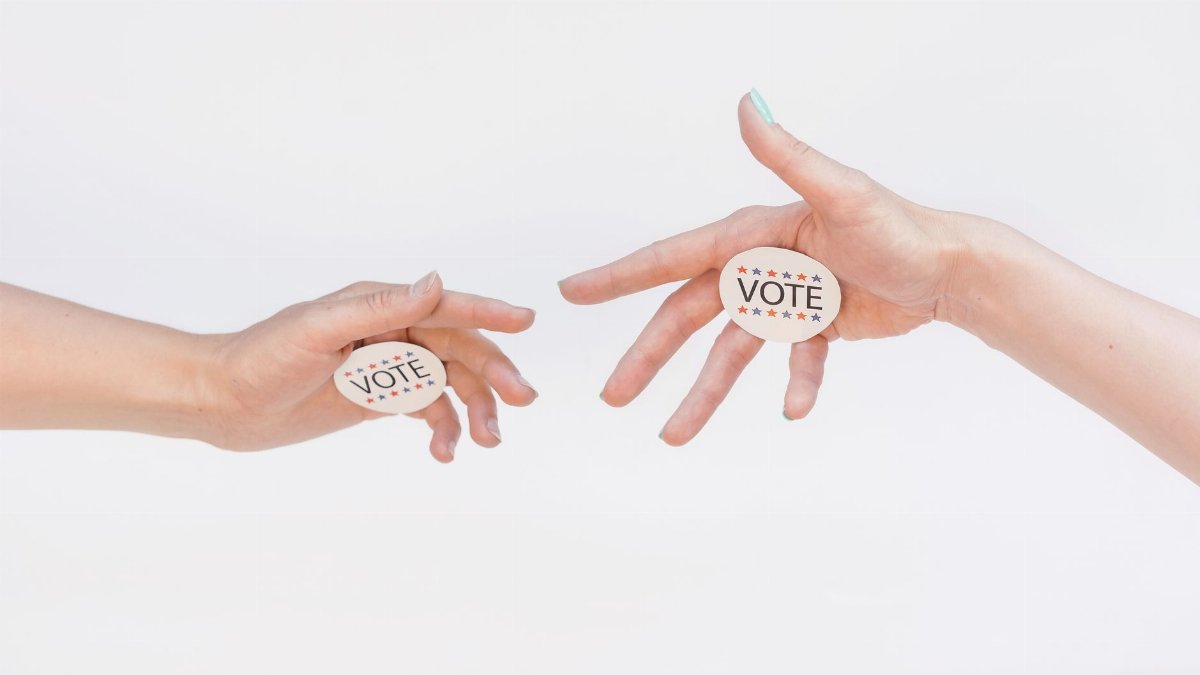 Two hands exchanging vote stickers symbolizing political participation and civic duty.