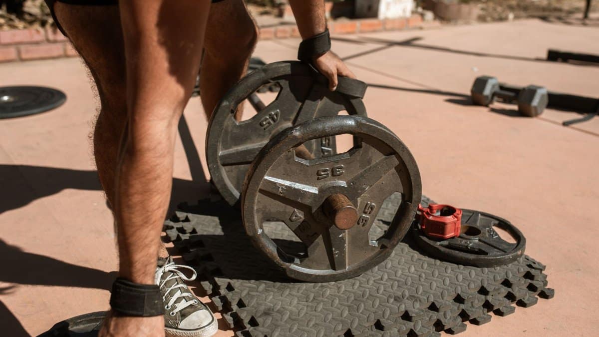 A man adjusts weight plates on a barbell during an outdoor workout session.