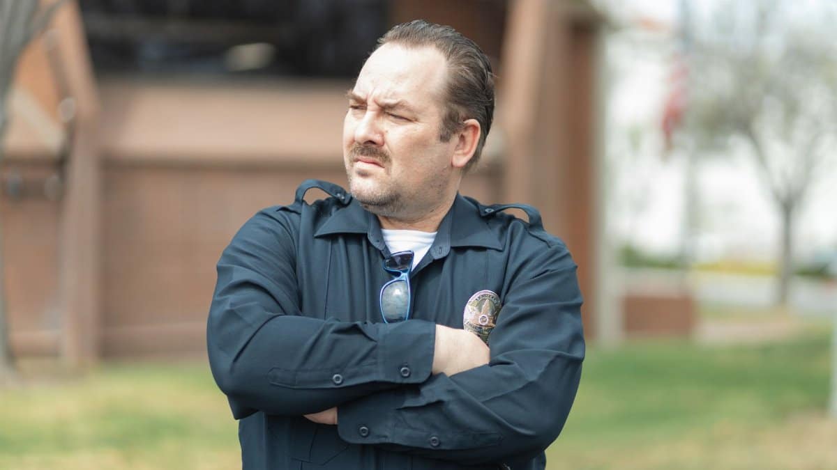 Law enforcement officer standing confidently with arms crossed outdoors in uniform.