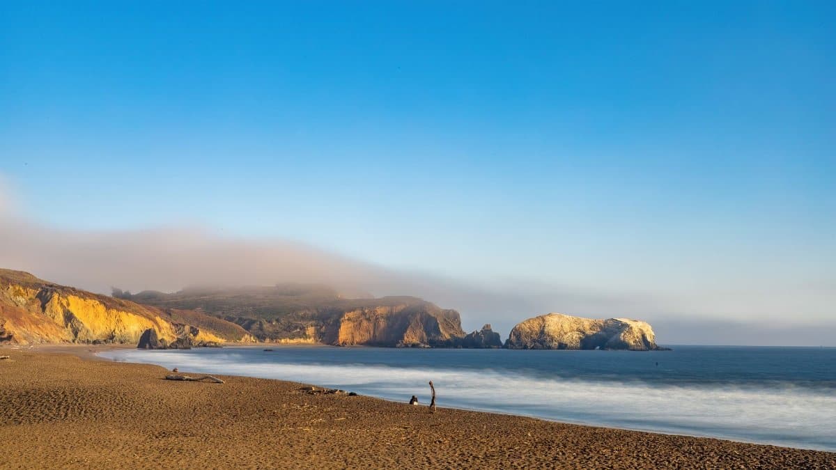 Breathtaking view of a serene beach with rocky cliffs under a clear blue sky.