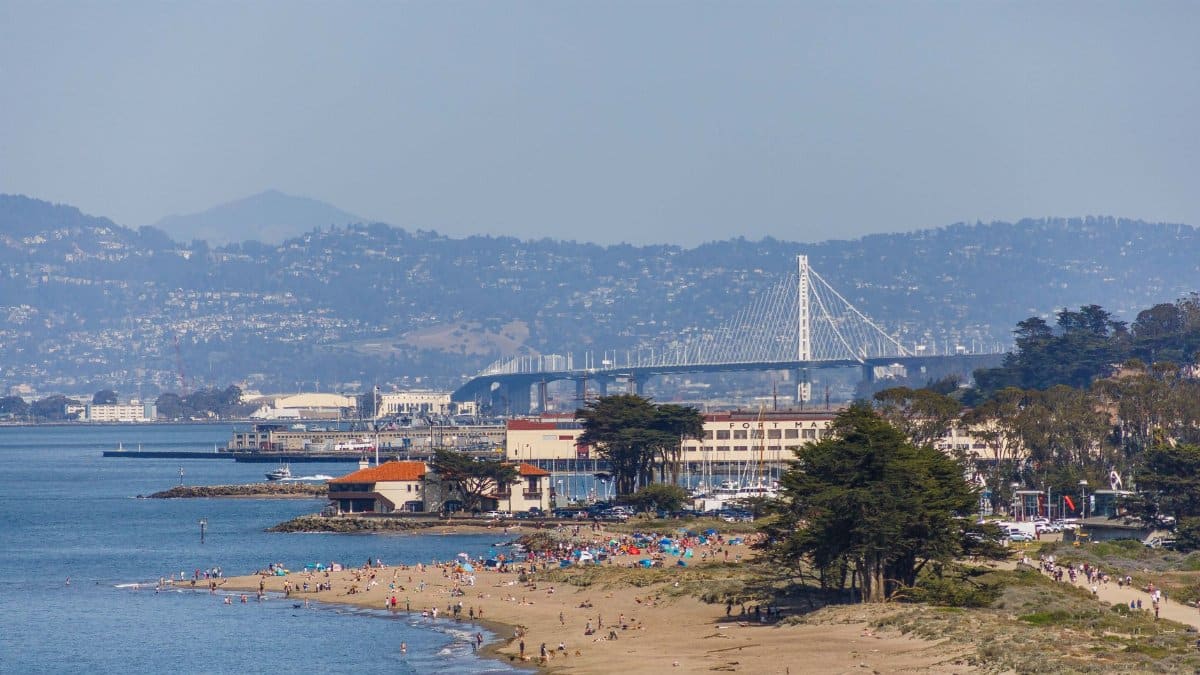A vibrant beach scene with San Francisco Bay Bridge in the background on a clear summer day.