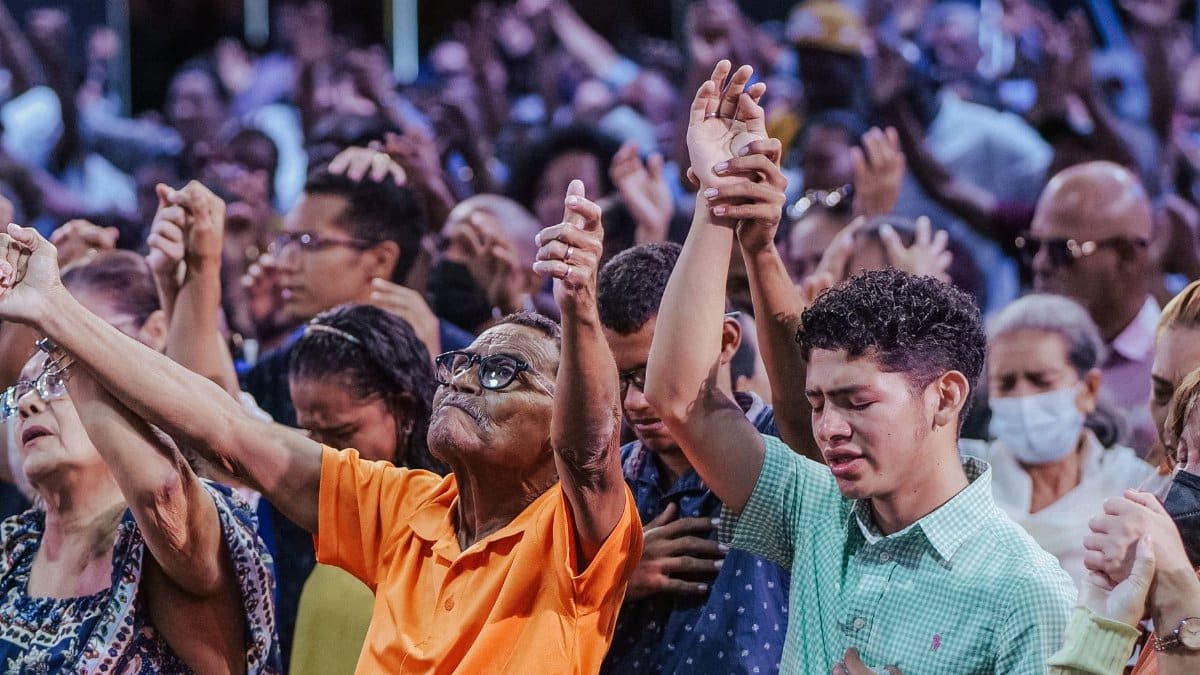 A diverse crowd engaged in a communal act of worship, raising hands in unity and prayer.