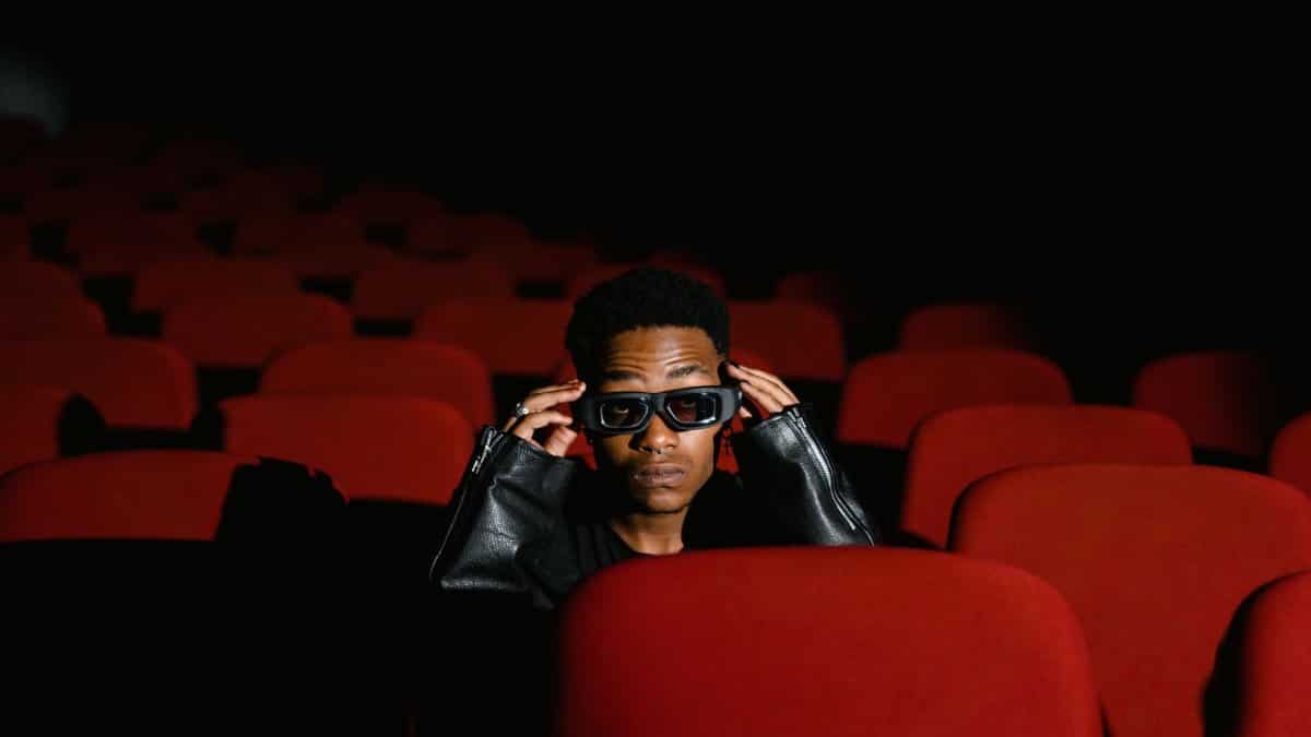 Individual sitting alone in a theater, wearing 3D glasses among red seats.