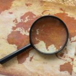 A top view of a vintage world map with a magnifying glass highlighting regions for exploration.