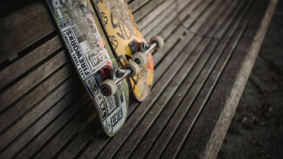 Boards with rollers for skateboarding placed on wooden bench in park in daylight