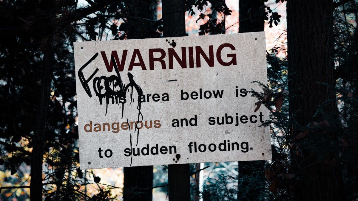A warning sign about sudden flooding amid a forest setting, emphasizing caution.