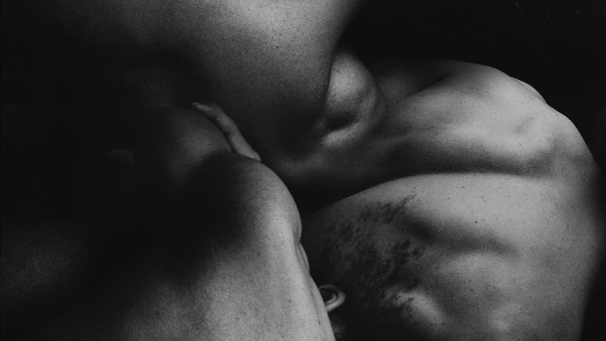 Abstract black and white photograph featuring the intertwined bodies of muscular men.