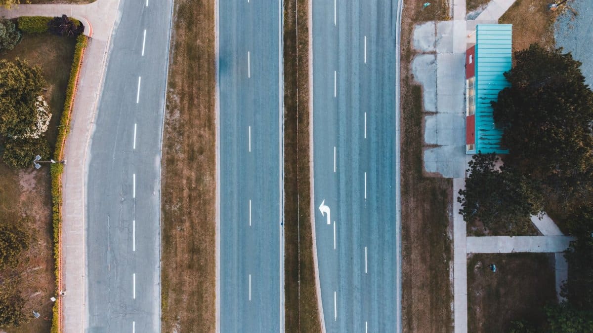 Bird's eye view of an empty urban two-lane highway with adjacent bus stop and greenery.