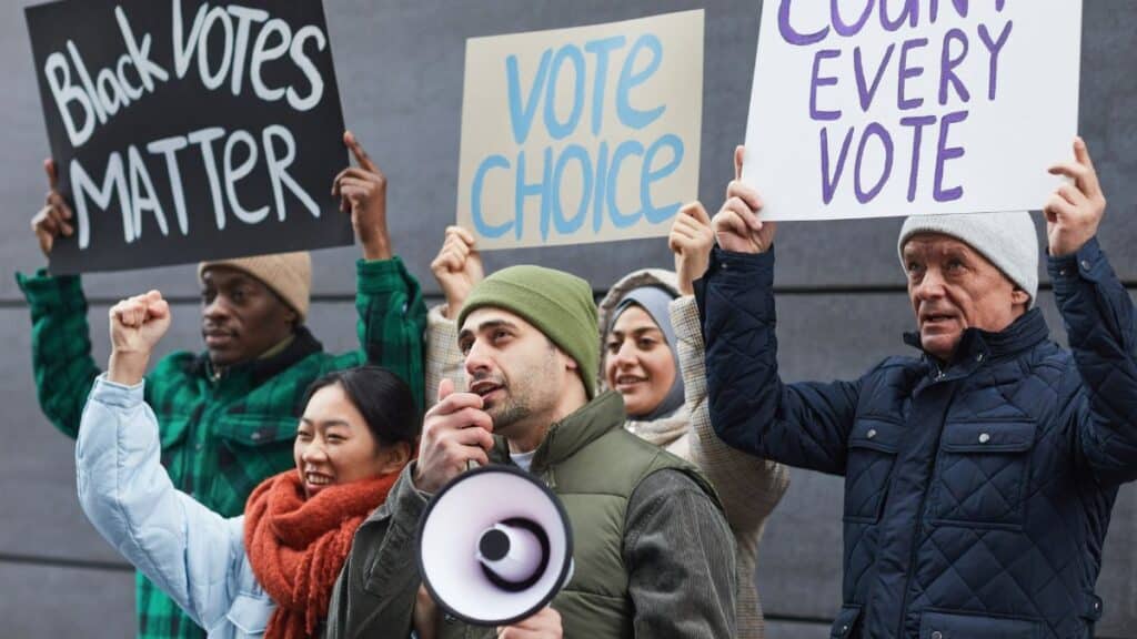 Group of diverse individuals protesting for voting rights with placards and megaphone.