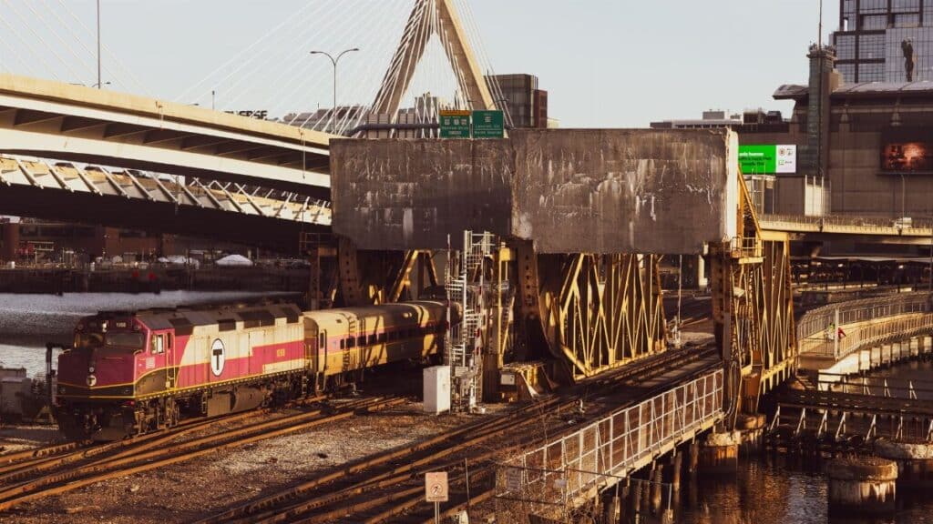 A train passes under the Leonard P. Zakim Bunker Hill Memorial Bridge in Boston during sunset.