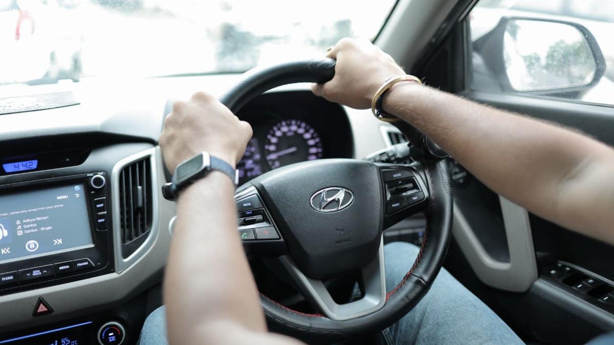 Close-up of a person driving a Hyundai car, showcasing hands on the steering wheel and dashboard detail.