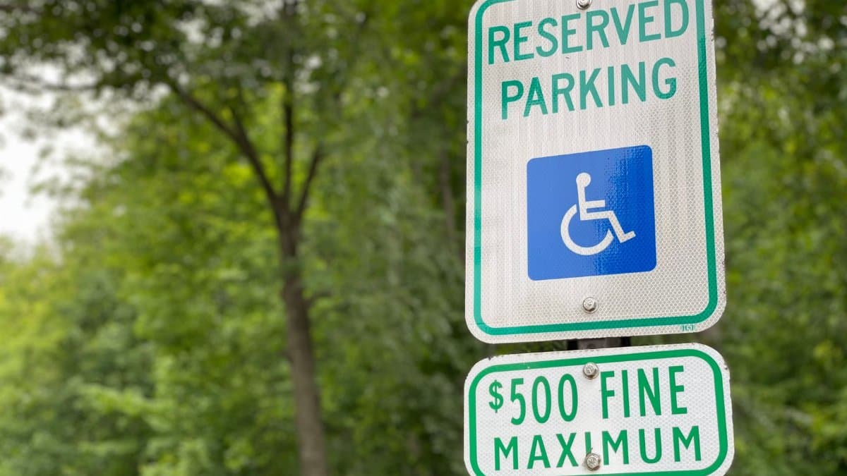 Close-up of a reserved parking sign with a fine notice, surrounded by lush greenery.
