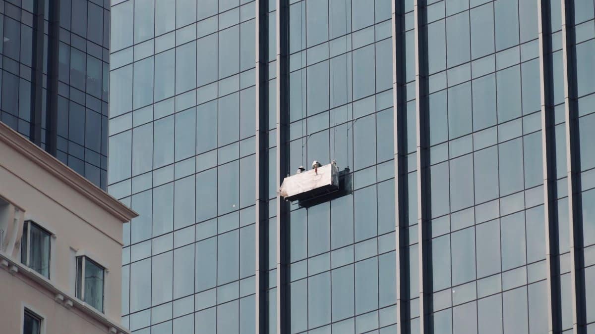 Two workers cleaning skyscraper windows on a suspended platform in an urban setting.