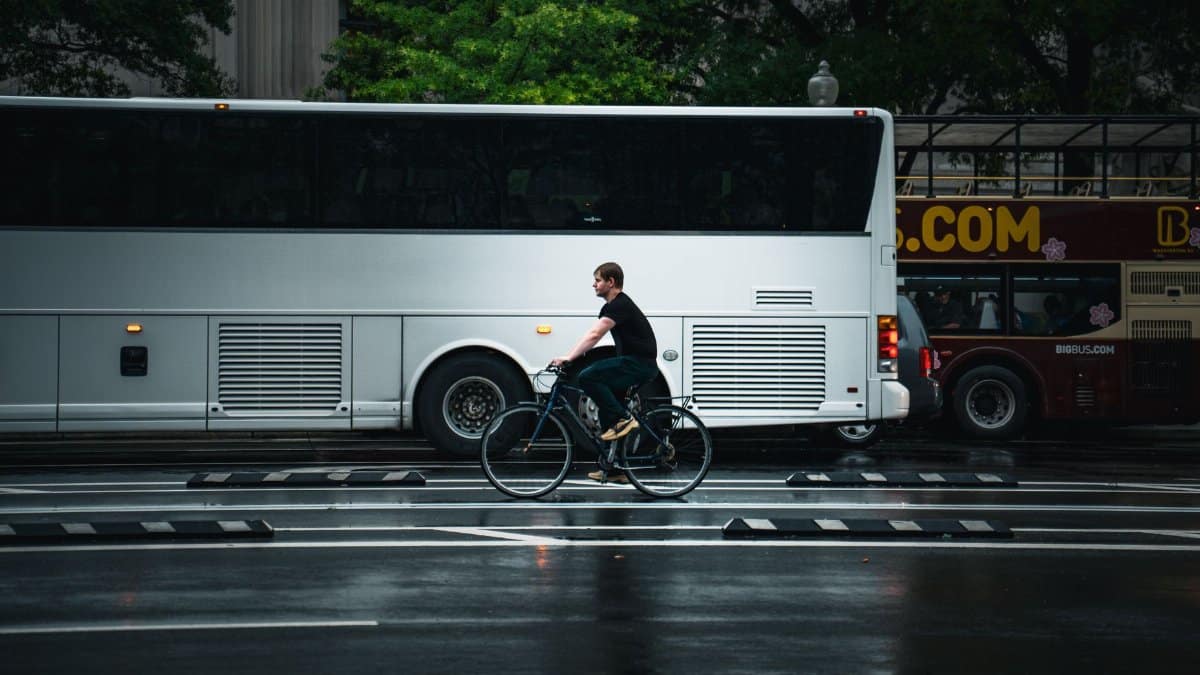 A cyclist rides past buses on a rainy Washington DC street capturing urban rhythm and motion.