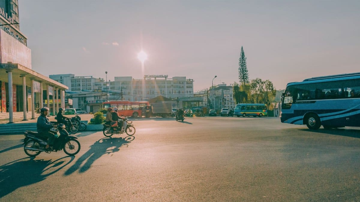 Urban street scene with motorcycles and buses during sunset, showcasing vibrant city life.