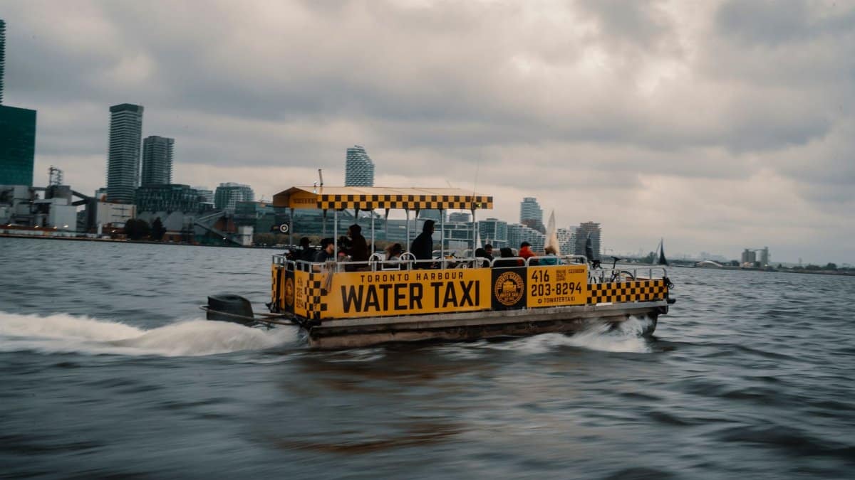 Water taxi navigating Toronto Harbour with city skyline in the background on a cloudy day.