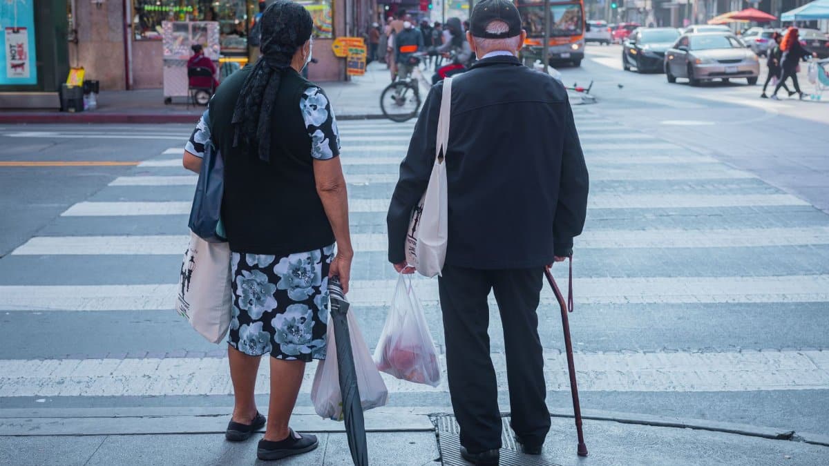Two senior adults crossing a busy street in downtown Los Angeles, showcasing urban life.