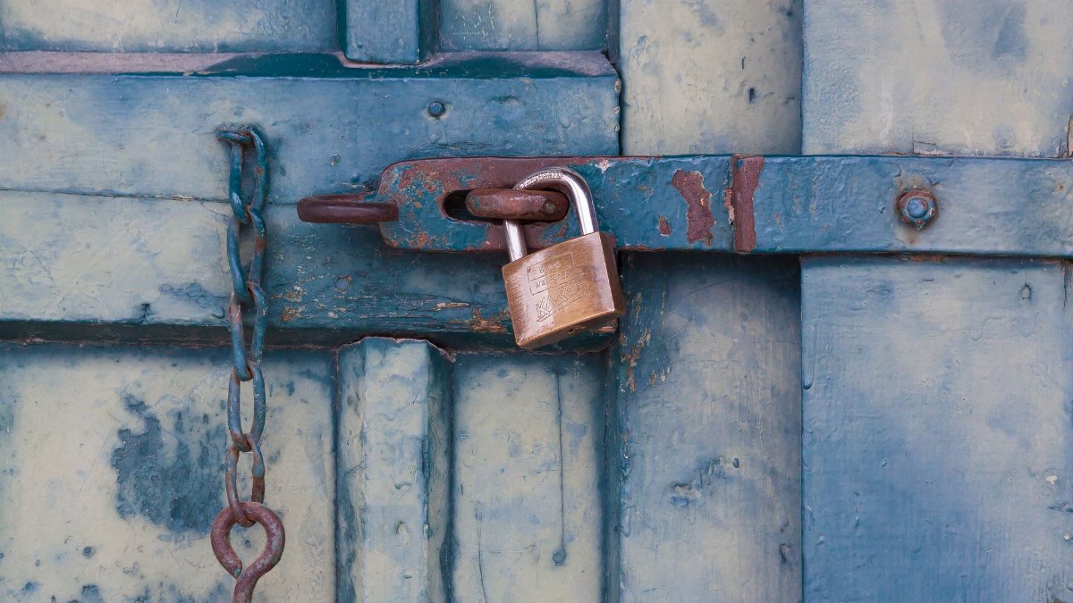 A close-up of a rusty padlock securing a blue painted wooden door with chain and bolt.